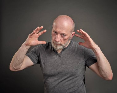 Kendine güvenen, ciddi ve odaklanmış yaşlı bir adamın portresi. Gri arka plana karşı anlamlı bir el hareketi.