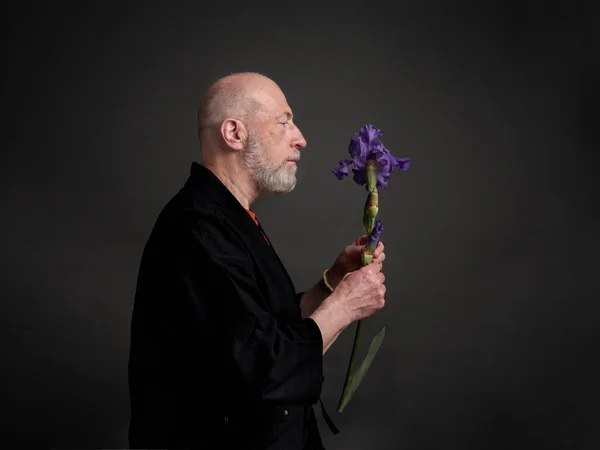 Head and shoulders profile portrait of bald and bearded senior man in kimono admiring an iris flower
