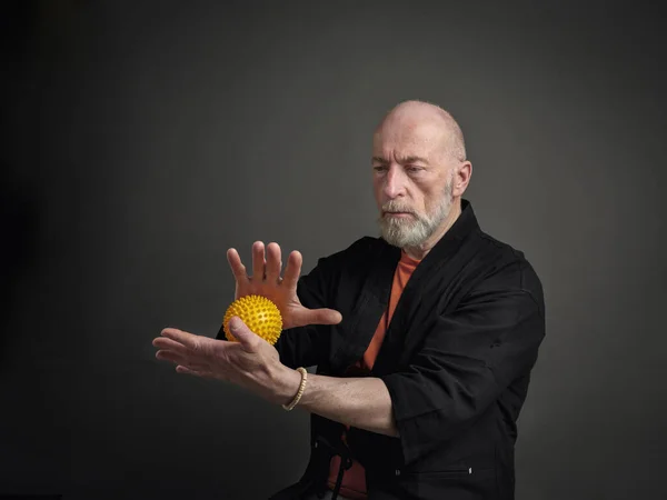 Head and shoulders portrait of bald and bearded senior man with a spiky self massage ball in his hands, self care concept
