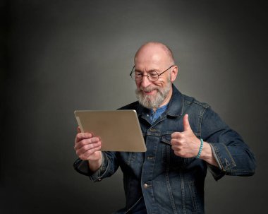 Gülümseyen ve olumlu kıdemli adam internette dijital tablet kullanarak sohbet ediyor.