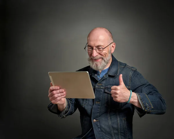 smiling and positive senior man is chatting online using a digital tablet, thumbs up hand gesture