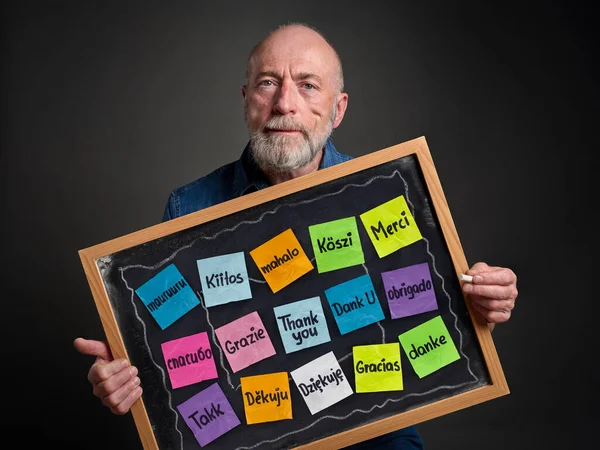 Thank you in sixteen languages - colorful sticky notes on blackboard held by a senior man