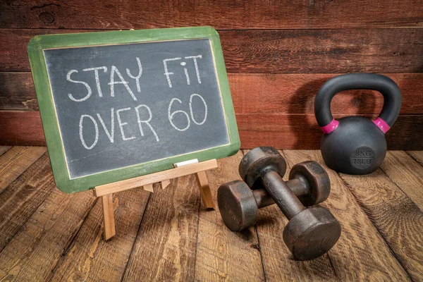 stay fit over 60 inspirational advice or reminder, white chalk text on a slate blackboard with dumbbells and kettlebell, aging and fitness concept