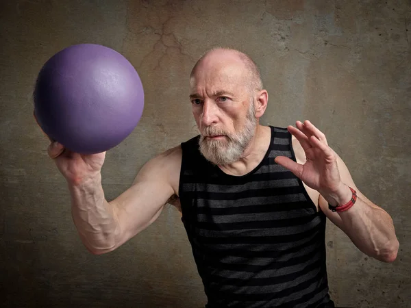 athletic senior man (late 60s) is exercising with a small medicine ball, fitness over 60 concept