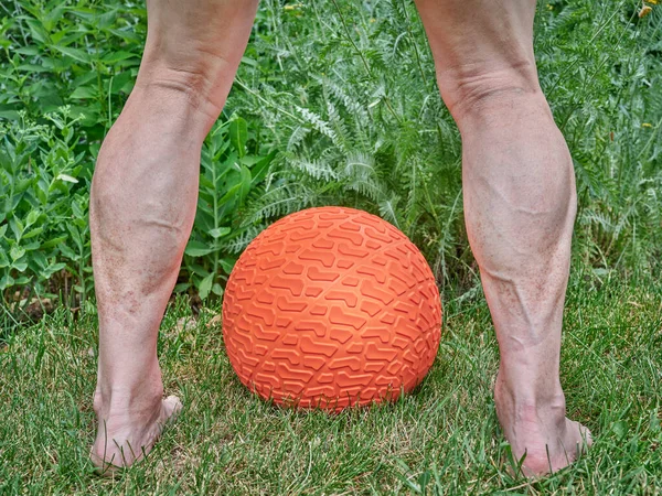 senior man legs and heavy rubber slam ball filled with sand in a backyard, exercise and functional fitness concept