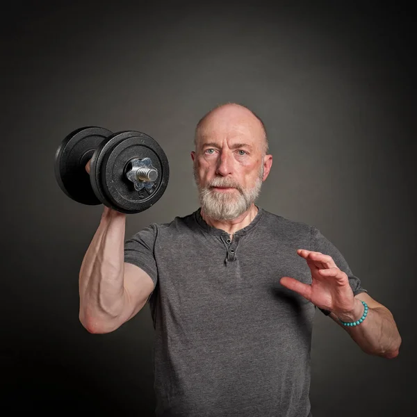 casual portrait of old bearded  man (in late 60s) exercising with heavy dumbbell, active senior and fitness concept