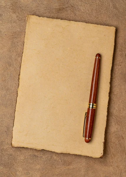 sheets of blank handmade paper with rough edges and a stylish pen against textured bark paper