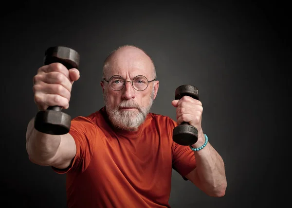 casual portrait of old bearded  man (in late 60s) exercising with small dumbbells, active senior and fitness concept