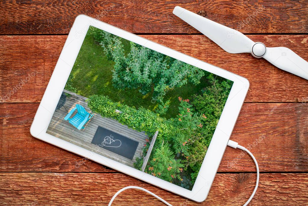 Adirondack chair, exercise mat and fitness jump rope on a wooden backyard deck, reviewing an aerial image of summer scenery on a digital tablet