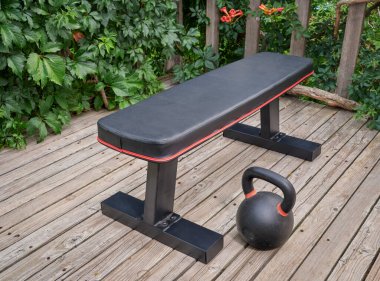 exercise bench and heavy iron kettlebell on wooden backyard deck