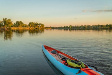 long and narrow racing stand up paddleboard with a paddle and safety leash on a calm lake at sunset.