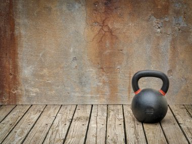 Kırsal bir ahşap zemin üzerinde demir kettlebell Bir kopya alanı ile grunge duvar karşı