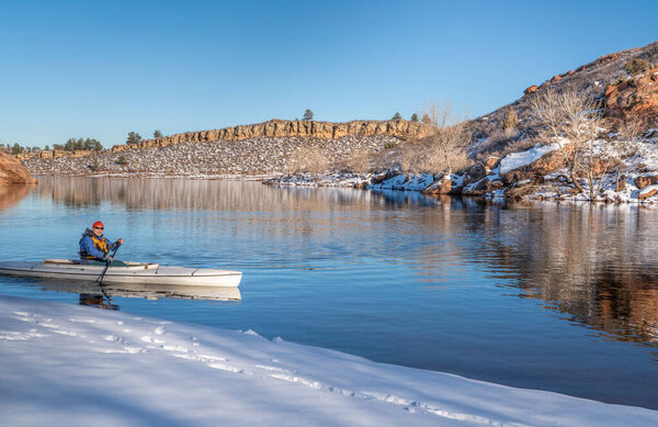 senior male wearing life jacket is paddling expedition canoe in winter scenery of Horsetooth Reservoir in northern Colorado