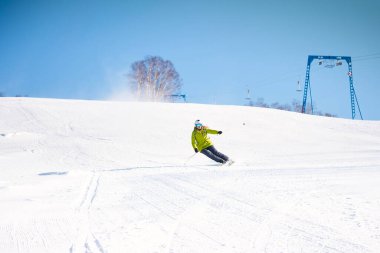Karlı dağların ve mavi gökyüzünün önünde yeşil ceketli neşeli kayakçı kız.