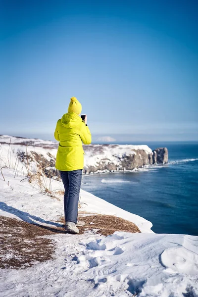 穿着绿色夹克的年轻女游客在太平洋边的电话里拍照 俄罗斯堪察加半岛 — 图库照片