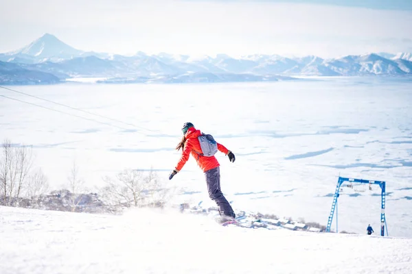 Snowboarder Dziewczyna Czerwonej Kurtce Jazdy Dół Wzgórza Przed Śnieżnymi Górami — Zdjęcie stockowe