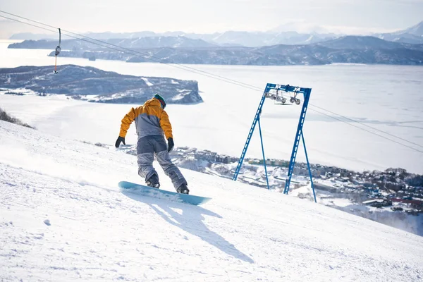 Snowboarder Jadący Dół Wzgórza Przed Lodowatym Oceanem — Zdjęcie stockowe