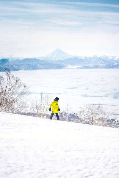 雪の山と青空の前の丘に乗って黄色のジャケットのスノーボーダーの女の子 ストック画像