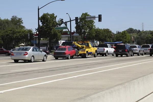 Caminhão de reboque amarelo puxando carro vermelho no trânsito — Fotografia de Stock