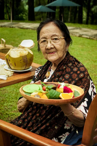 Happy Southeast Asian old woman with a tray full of food in hand at the tropical resort