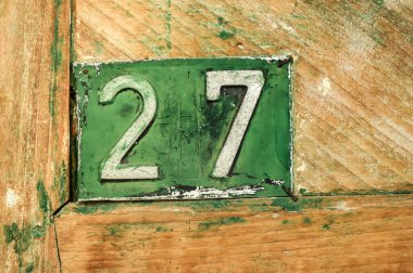 Kırsal bir ahşap kapıda yeşil renkli eski ev plakası.