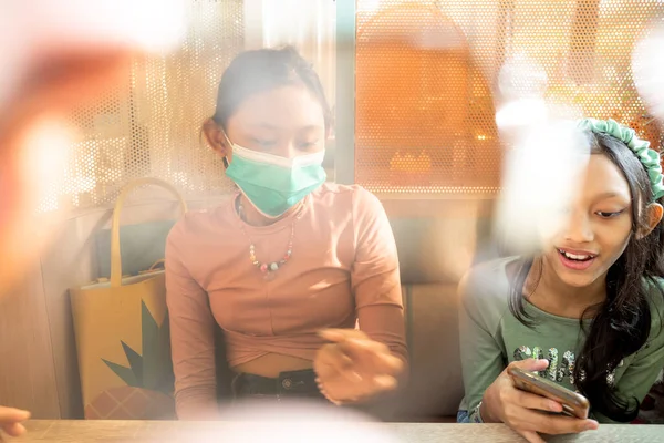 两名东南亚少女一起在一家餐馆里鬼混 其中一人戴着面具 — 图库照片