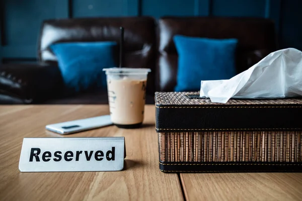 A Cup of Iced Coffee on a Reserved Table at Restaurant with Leather Sofa on the Background