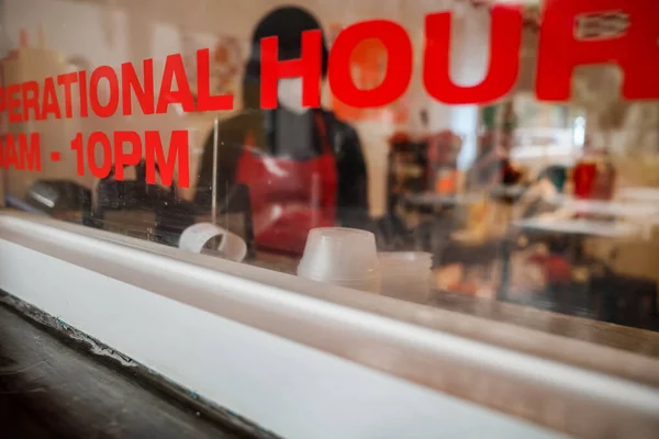 Restaurant operational hour displayed on cashier window with female employee on the background