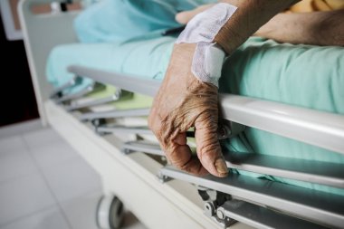Wrinkled hand of a female elderly patient on the handrail of a hospital ward