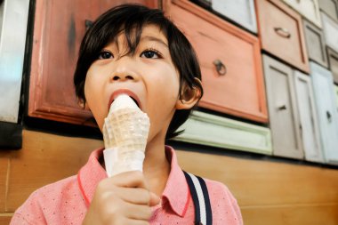 Southeast Asian boy enjoying eating vanilla ice cream cone at mall