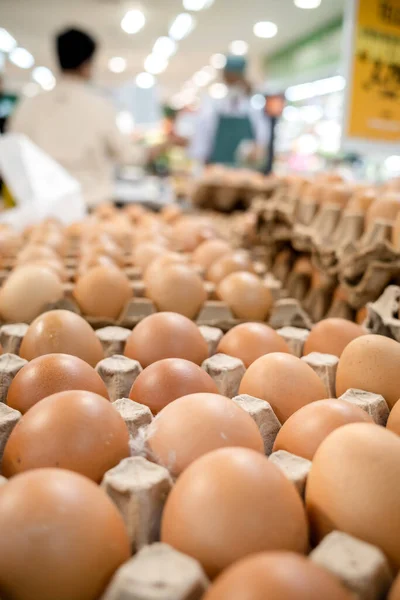 Chicken eggs on trays for sale in a supermarket with buyer and staff on the background