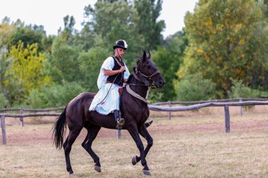 Hortobeage, Hungary, Aug. 04. 2021: Geleneksel halk kostümlü Macar kaçıklar eğitimli atını gösteriyor. Macaristan, Hortobagy, Macaristan 'ın geleneksel at çobanı
