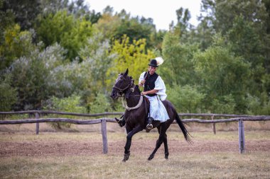 Hortobeage, Hungary, Aug. 04. 2021: Geleneksel halk kostümlü Macar kaçıklar eğitimli atını gösteriyor. Macaristan, Hortobagy, Macaristan 'ın geleneksel at çobanı