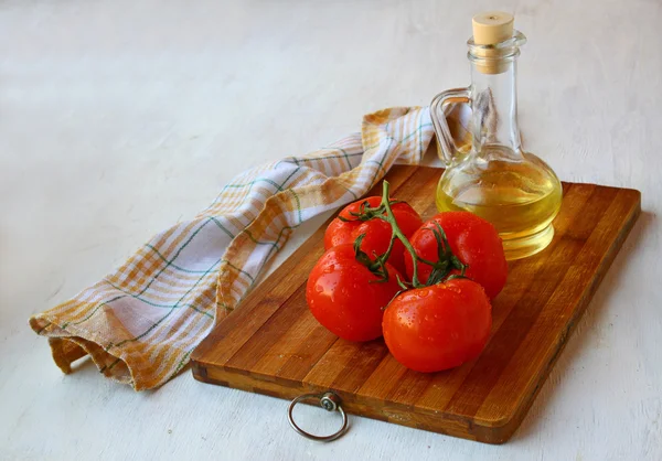 Bunch of tomato on the board and the bottle of olive oil — Stock Photo, Image