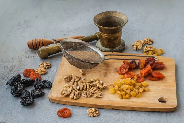 Dried fruits, sieve, brass mortar, honey spoon on a cutting board.