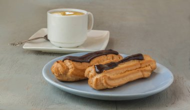 Gri arka planda iki çikolatalı ekler ve bir fincan espresso kahvesi. Sığ alan derinliği, eklerlere odaklan