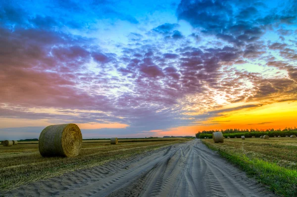 Pôr do sol sobre estrada rural e fardos de feno — Fotografia de Stock