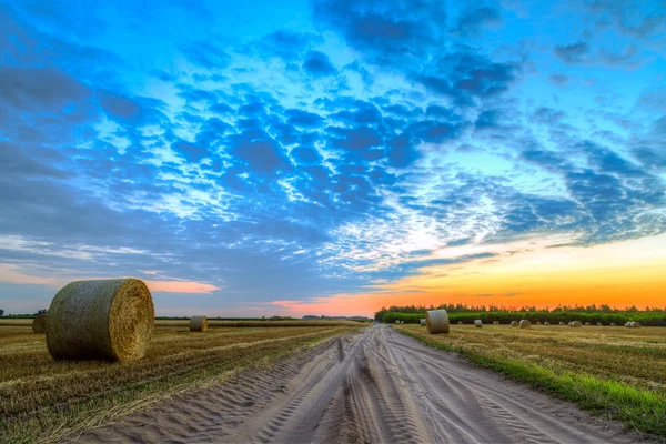 Tramonto su strada rurale e balle di fieno — Foto Stock