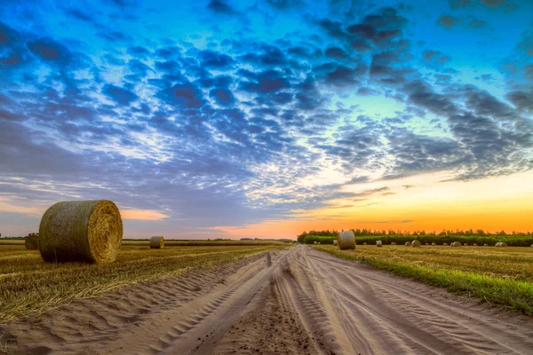 Pôr do sol sobre estrada rural e fardos de feno — Fotografia de Stock