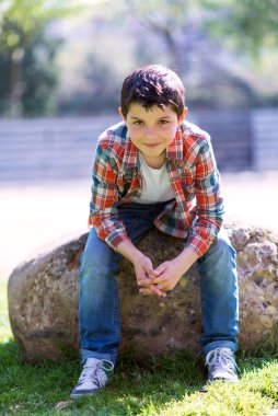 Şehir parkında kayalıklarda otururken günlük kıyafetler giyen gülümseyen çocuk.