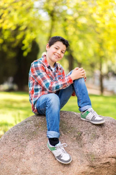 Sonriente Niño Usando Ropa Casual Mientras Está Sentado Roca Parque —  Fotos de Stock