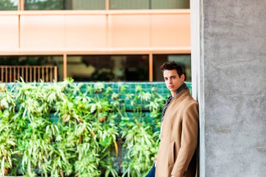 Dışarıda duran ve duvara yaslanan şık ve yakışıklı genç adamın portresi..