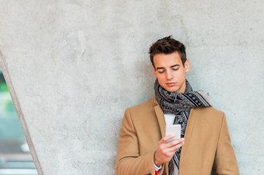Şehrin duvarına yaslanmış akıllı telefon kullanan neşeli bir adam.