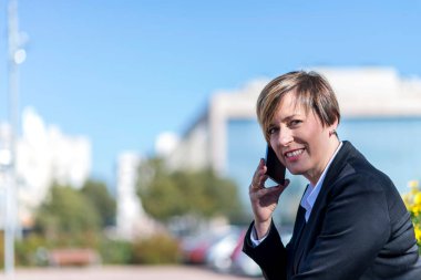 İspanyol iş kadını gülümsüyor dışarıda bir cep telefonundan konuşuyor.