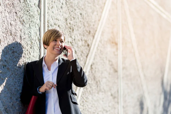 İspanyol iş kadını gülümsüyor dışarıda bir cep telefonundan konuşuyor.