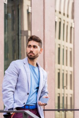 Sakallı erkek, dışarı bakarken cep telefonu tutuyor.