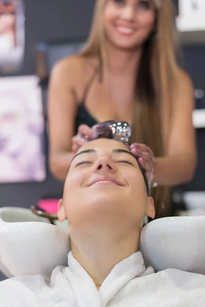Front view of a hairdresser washing hair of a beautiful young lady in hair salon.