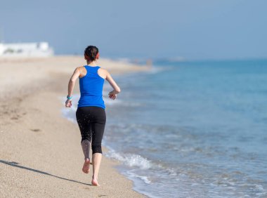Genç bir kadın sabahları kumsalda koşar.