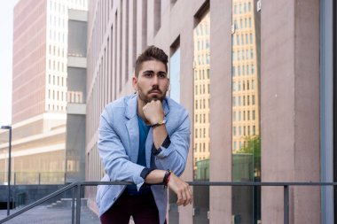 Portrait of a young man leaning on railings outdoor while looking to camera