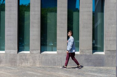 Businessman walking next to office buildings while holding a shoulder bag